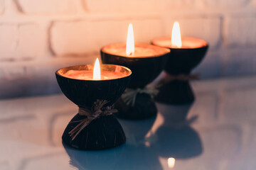 Burning spa aroma candles in coconut shell on a glass white table, cozy home interior.