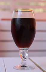 A glass of cold dark beer on a white wooden table in cafe. The glass is covered with small water droplets. Concept of hot summer thirst quenching, relaxation and fun, drinking beverages
