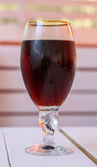 A glass of cold dark beer on a white wooden table in cafe. The glass is covered with small water droplets. Concept of hot summer thirst quenching, relaxation and fun, drinking beverages