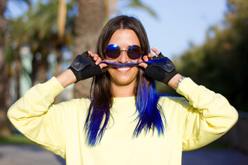 A portrait of beautiful carefree girl with blue hair in yellow top and retro sunglasses in the park...