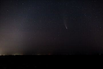 Comet NEOWISE in the dark starry sky above the horizon at night. Horizontal orientation. 