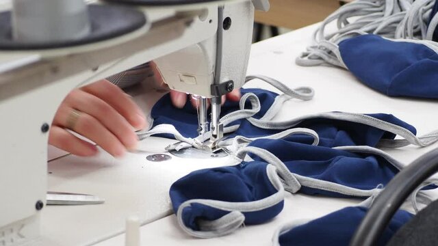 The process of covid-19 protective masks sewing on the overlock in the sewing shop. Close up of sewing process on the overlock in the sewing shop. Tailoring industry..