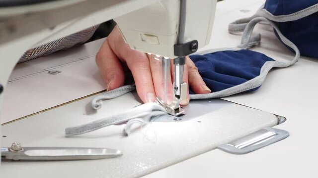 The process of covid-19 protective masks sewing on the overlock in the sewing shop. Close up of sewing process on the overlock in the sewing shop. Tailoring industry..