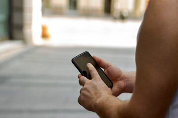 Close-up image of male hands using smartphone during summer day on city shopping street,searching or social networks concept,hipster man typing sms message to his friends.Technology lifestyle concept.