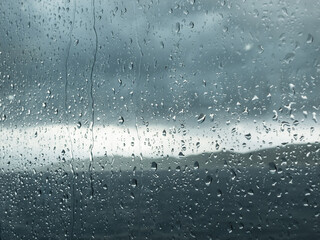 Rainy window with heavy gray clouds and blurred mountain landscape outside.