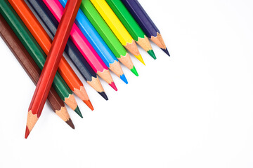 One red color wood pencil crayon placed on top of a row of different color wood pencil