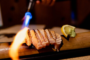 Kitchen torch burn on salmon on bamboo dish. Burn on salmon sashimi. Selectived focus. Japanese...