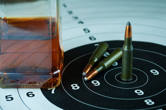 gun casings with a glass of whiskey and a bottle on a wooden table and a target