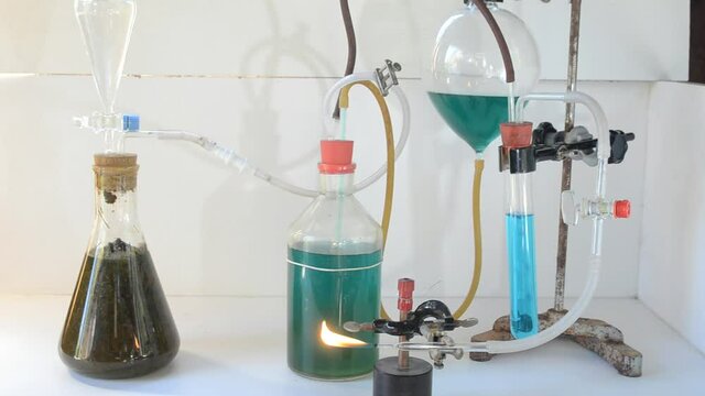 Small rig to make biogas,  left reactor with biomass, then two flasks with green water for pressure regulation, a test tube with blue water to prevent backfire in unclean gas, and finaly the gas flame