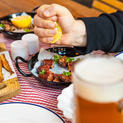 Man squeezing lemon on the meat meal with beer