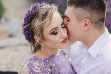 Young couple in love kissing in a lavender field on summer clody day. girl in a luxurious purple dress and with hairstyle