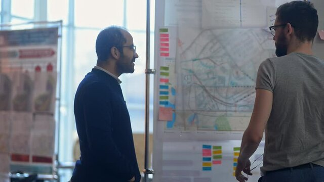 Designer presenting his ideas on a whiteboard to colleague. lrrl in creative office. architect man develop new map of the city and shoe explain it to boss coworker