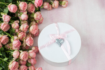 On a pink background, a bouquet of pink roses and a gift in a box