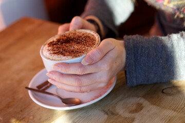 Hands holding a cup with white saucer,