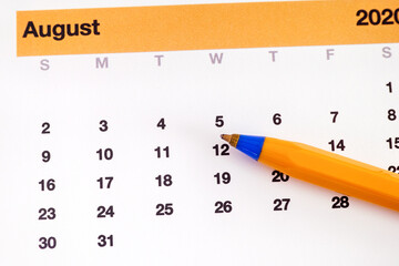 A ballpoint pen lying on a calendar that is showing august month