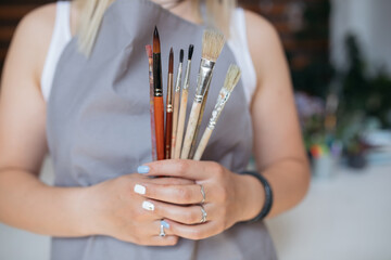 Young female artist holding paintbrushes to draw in art studio.