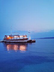 Fototapeta premium one passenger sea boat on the pier on a summer evening against the background of the blue sea and blue sky.travel.waterscape.vertical orientation.Trend of the year classic blue.