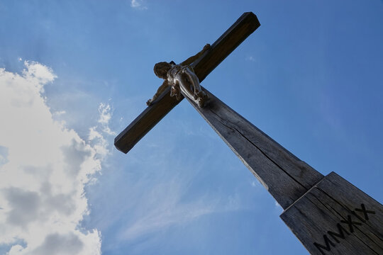 Jesus figure ( cruci fixus ) on brown wooden cross. Picture was taken diagonally from below. Blue sky with white clouds. Germany.