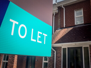 Estate agency 'To Let' sign board with large typical British houses in the background
