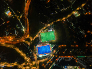 Aerial bird’s eye view of the outdoor hockey field at night. The image contains soft-focus, grain, and noise.