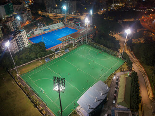 Aerial bird’s eye view of the outdoor hockey field at night. The image contains soft-focus, grain, and noise.