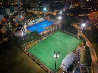 Aerial bird’s eye view of the outdoor hockey field at night. The image contains soft-focus, grain, and noise.