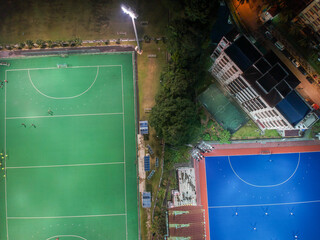 Aerial bird’s eye view of the outdoor hockey field at night. The image contains soft-focus, grain, and noise.