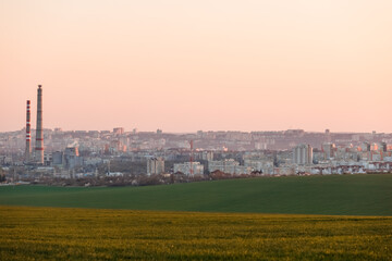 A shot of a beautiful city and a green plain during sunset.