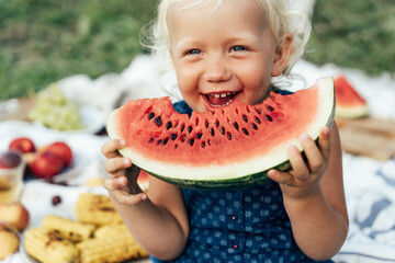 Cute toddler girl eating watermelon on a picnic outside in summer. Spending time in pleasure. Children's  immediate emotions. Innocence and a happy cheerful kid