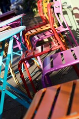 Brightly coloured metal tables and chairs outside a cafe in the sunshine,