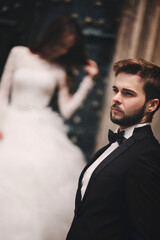 Wedding couple near the vintage green door. Stone walls in ancient town background. bride with long hair in lace dress and groom in suit and bow tie. Tender embrace. Romantic love