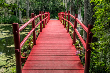 A beautiful red foot bridge crosses a pond in an idyllic plantation landscape near Charleston, South Carolina.