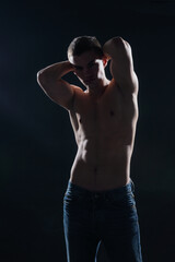 High contrast silhouette portrait of a sexy young male model shirtless posing on the side.