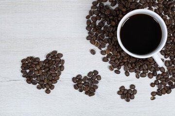 Grains of coffee with a cup of coffee on a background of bleached wood.
