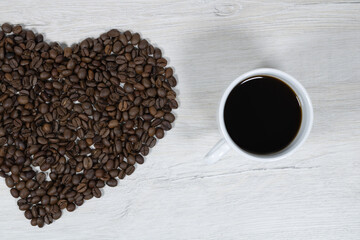 Grains of coffee with a cup of coffee on a background of bleached wood.
