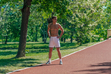 Young athlete without t-shirt is standing on a running track in the park