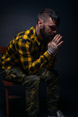 Fototapeta premium Close up portait of a male model with tattoos and tartan shirt sitting on a chair isolated on a black background