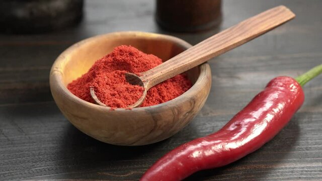 Red chili powder or paprika in a wooden bowl on table close-up. Cooking ingredients.