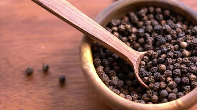 Black peppercorns in bowl with spoon, rotation