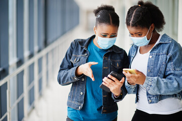 Two african woman friends in jeans jacket wearing protective masks with mobile phones. Virus concept health, medical.