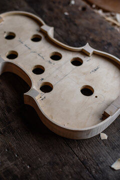 High angle of wooden soundboard with round holes and attached shells on workbench with sawdust in workshop