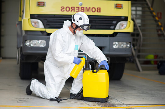 Side view of fireman in protective costume and respirator pouring liquid in plastic container for disinfection of fire station during coronavirus pandemic