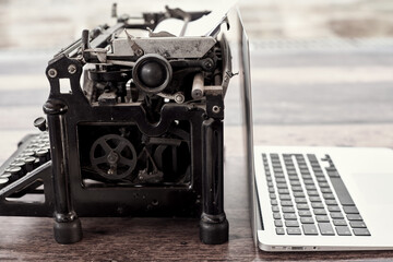 Modern netbook and old fashioned typewriter placed on wooden table on terrace