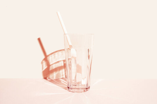 Glass for cocktail with plastic straw placed on pink background in studio