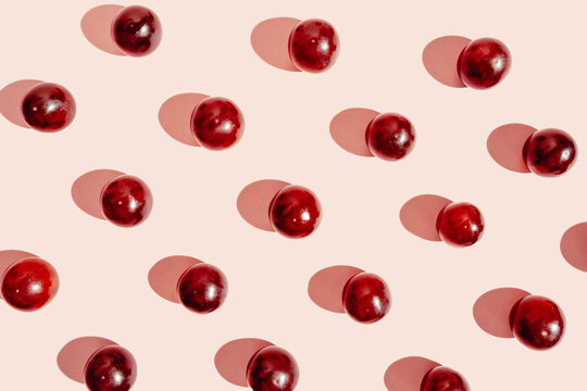 Top view of pattern of fresh red grapes arranged in lines on pink surface in studio
