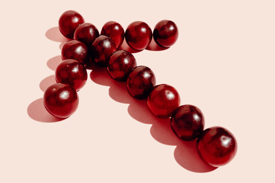 Top view of red grapes arranged in arrow showing direction on pink background