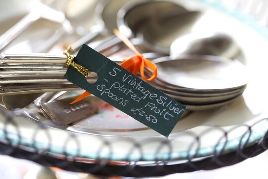 Vintage Fruit Spoons Tied With An Orange Ribbon On A Cake Stand With A For Sale Sign In Black And With White Writing,