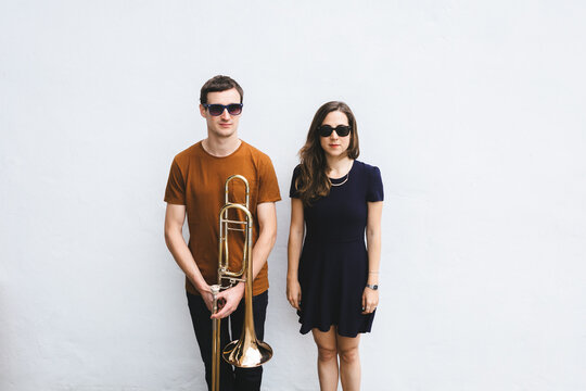 Stylish boyfriend with trombone standing near girlfriend against a white wall