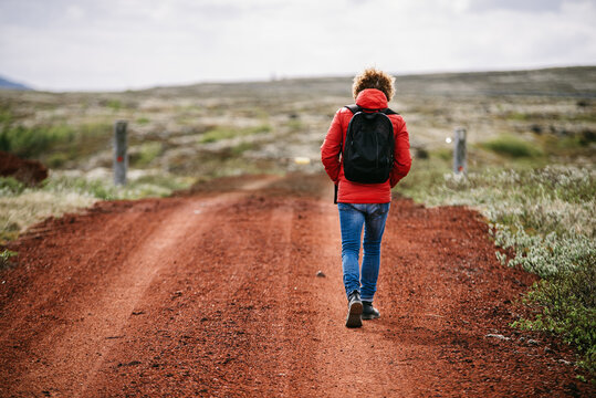 Back view of traveling man in outerwear walking along sandy road during vacation in Iceland
