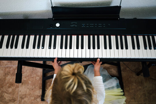 From above unrecognizable focused blond little girl playing synthesizer at home